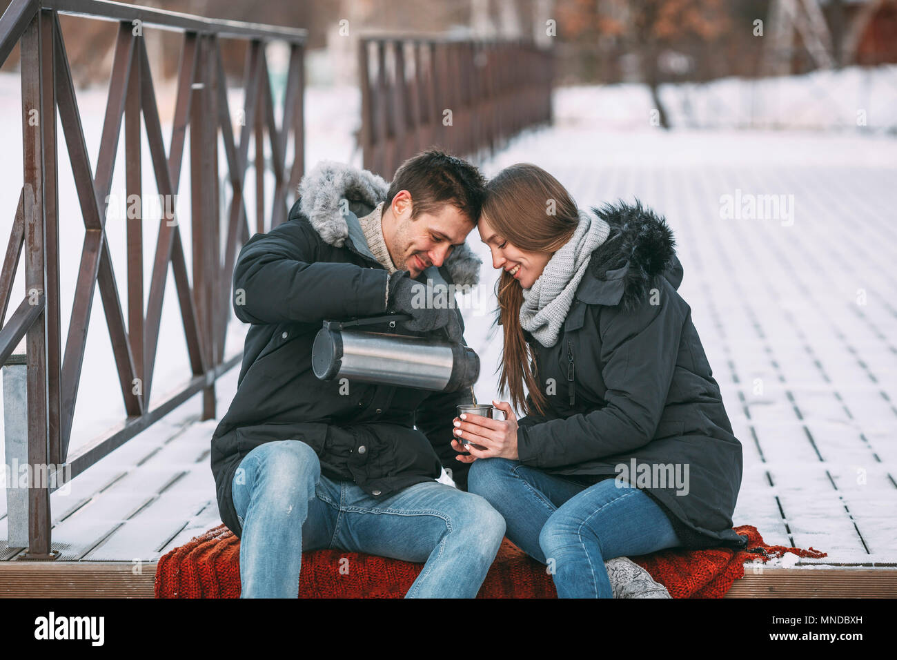 Glückliche Menschen gießen Drink von isolierten Behälter auf der Promenade im Winter Stockfoto
