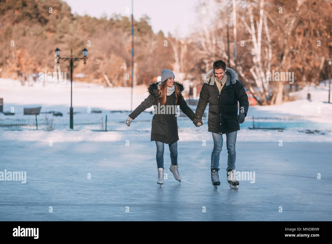 Volle Länge des glücklichen Paare halten sich an den Händen, während sie Eislaufen auf der Eisbahn Stockfoto