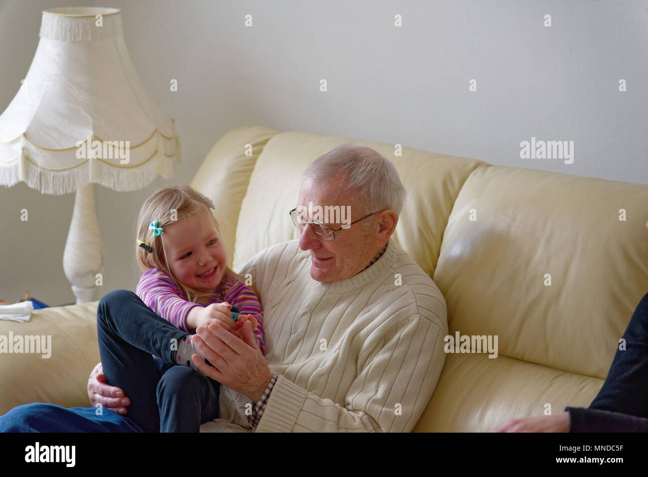 Großvater und seine drei Jahre alte Enkelin zusammen lachen setzte sich auf ein Sofa Stockfoto