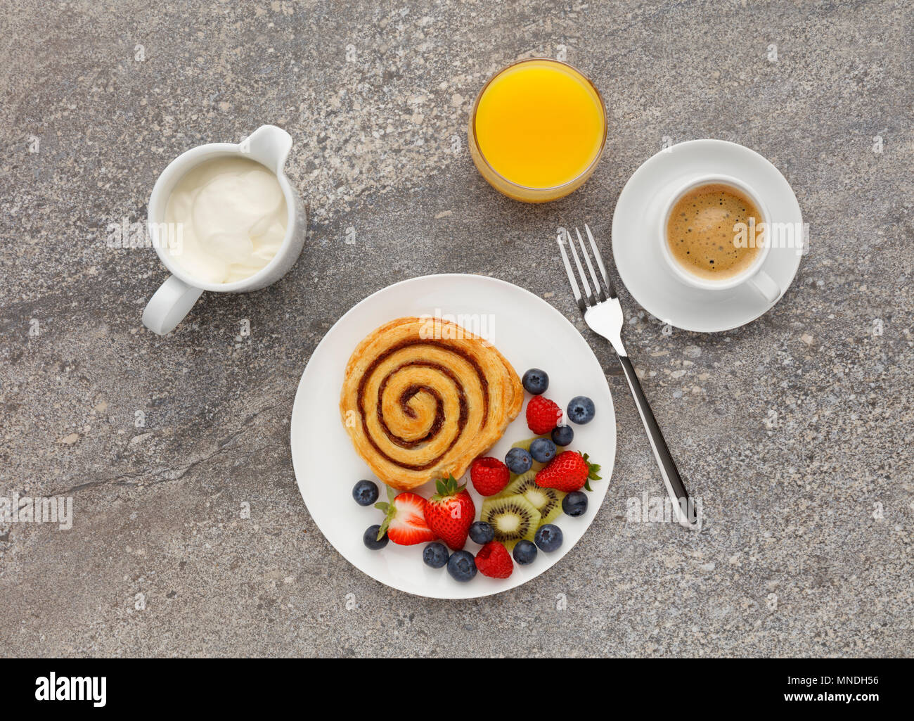 Kontinentales Frühstück mit einem Cinnamon Swirl, Obst, Kaffee und Orangensaft, Schuß auf einen Stein Küche Arbeitsplatte, von oben. Stockfoto