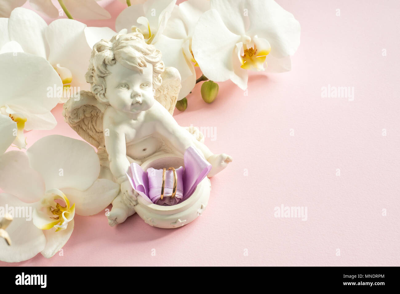 Weiße Orchidee Engel Skulptur Trauringe auf rosa Hintergrund. Stockfoto