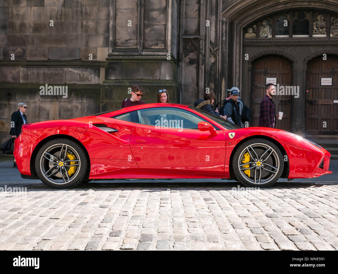Royal Mile, Edinburgh, Schottland, Vereinigtes Königreich, Mai 2018. Leute, die von einem hellen roten Ferrari 488 GTB coupé Sportwagen auf einer doppelten gelben Linie auf dem gepflasterten Royal Mile geparkt neben der St. Giles Cathedral, die neidvolle Blicke Stockfoto