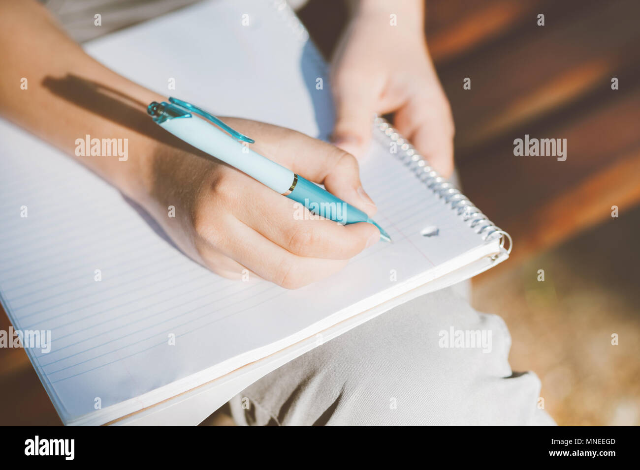 Nahaufnahme auf Boy's Hände schreiben im Notebook outdoor. Teenager sitzen auf einer Holzbank und seine Hausaufgaben machen. Stockfoto