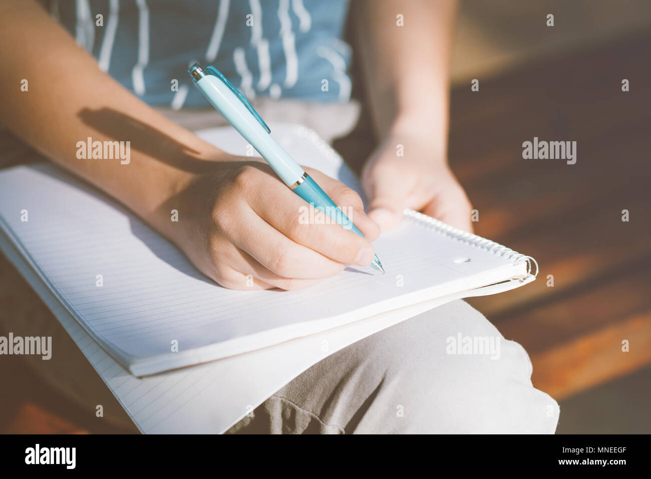 Nahaufnahme auf Boy's Hände schreiben im Notebook outdoor. Teenager sitzen auf einer Holzbank und seine Hausaufgaben machen. Stockfoto