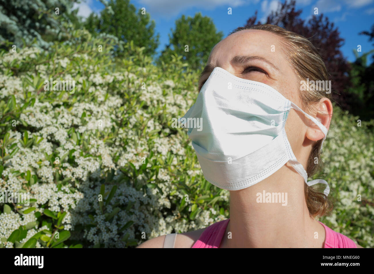 Junge Frau mit Schutzmaske in blühenden Park mit halb geschlossenen Augen wegen der starken Sonne Stockfoto