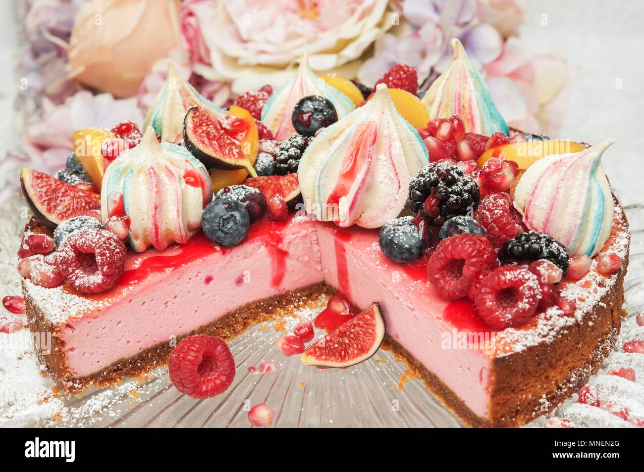 Strawberry Cheesecake mit merangue Küsse und frisches Obst an der Oberseite auf einem Glas Kuchen stehen vor Blumen Stockfoto