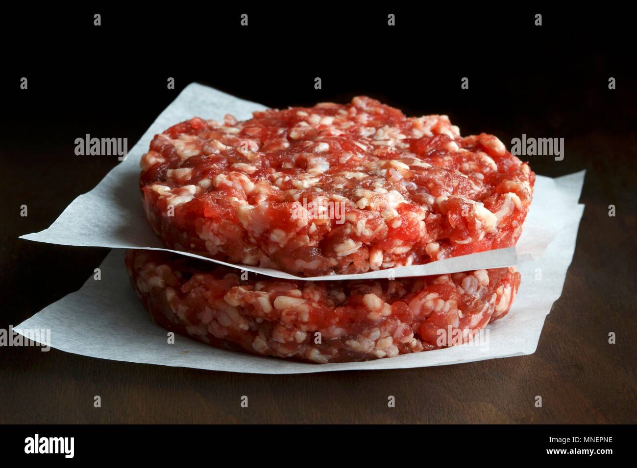 Zwei rohe hand made Beef Burger Pastetchen auf weißem Wachs Papier dunklen Hintergrund gestapelt Stockfoto