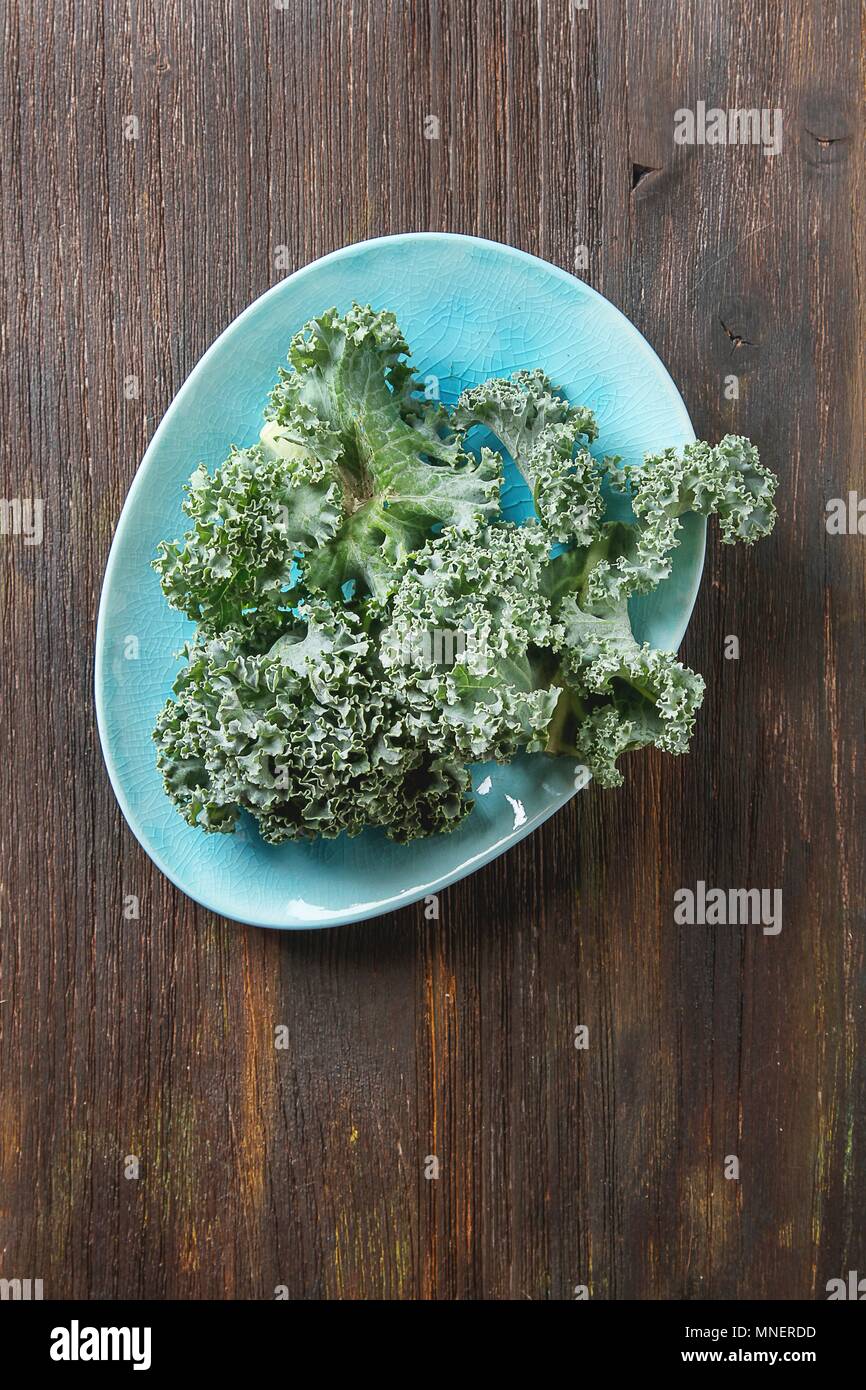 Frischen Grünkohl Blätter auf einem blauen Platte auf einer hölzernen Oberfläche Stockfoto