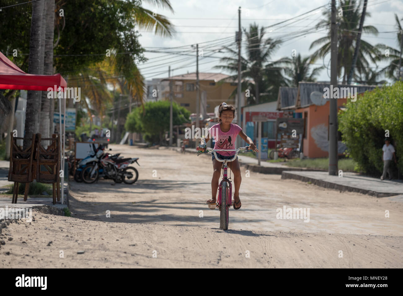 Ecuadorianischen Mädchen mit dem Fahrrad auf einem sand Straße in Puerto Villamil, Isabela Island, Galapagos, Ecuador. Stockfoto
