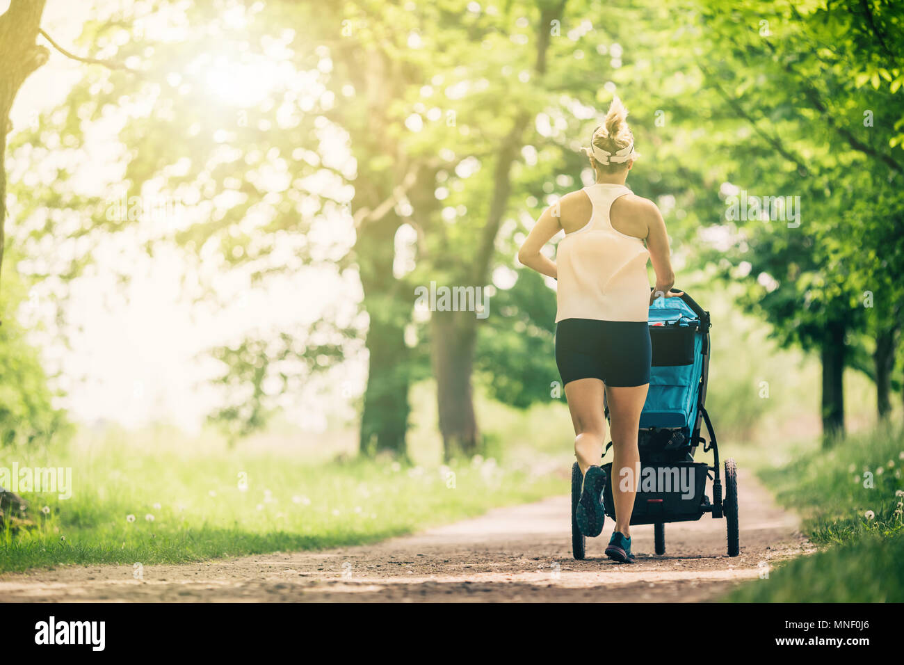 Läuft eine Frau mit Kinderwagen geniessen Sommertag im Park. Joggen oder Walken supermom, aktive Familie mit Baby Jogger. Stockfoto