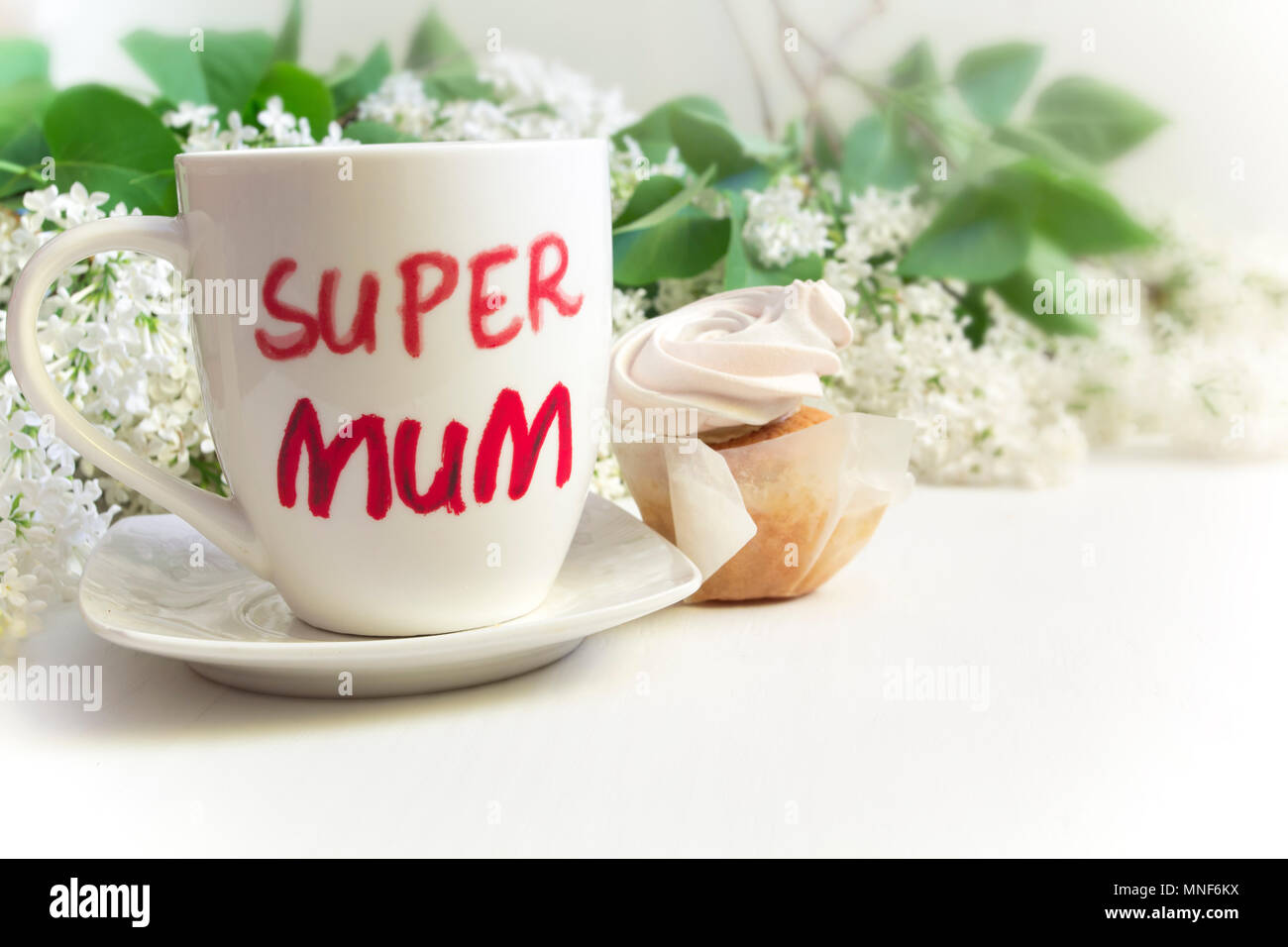Muttertag Konzept. Tasse mit der Aufschrift "Super Mama", cupcake und lila Blüten. Stockfoto