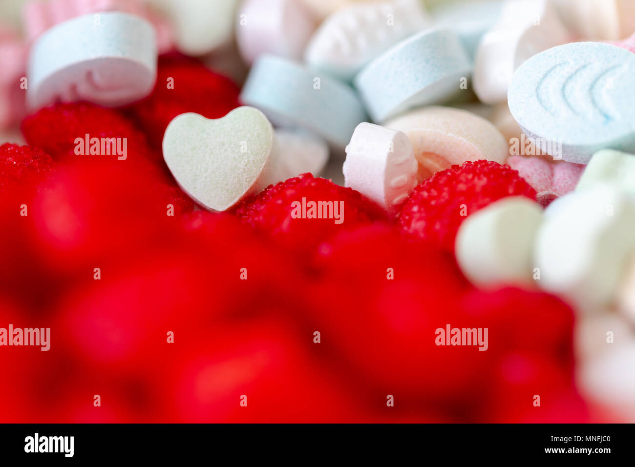 Süße Pillen und Tropfen in lebendigen Farben. Selektiver Fokus auf Herz Form Pille. Full Frame Hintergrund Stockfoto