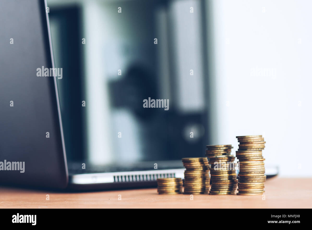 Gestapelte Säulen von Geld Münzen und Laptop Im defokussierten Hintergrund für Finanzen, Wirtschaft und Budgetierung Konzept Stockfoto