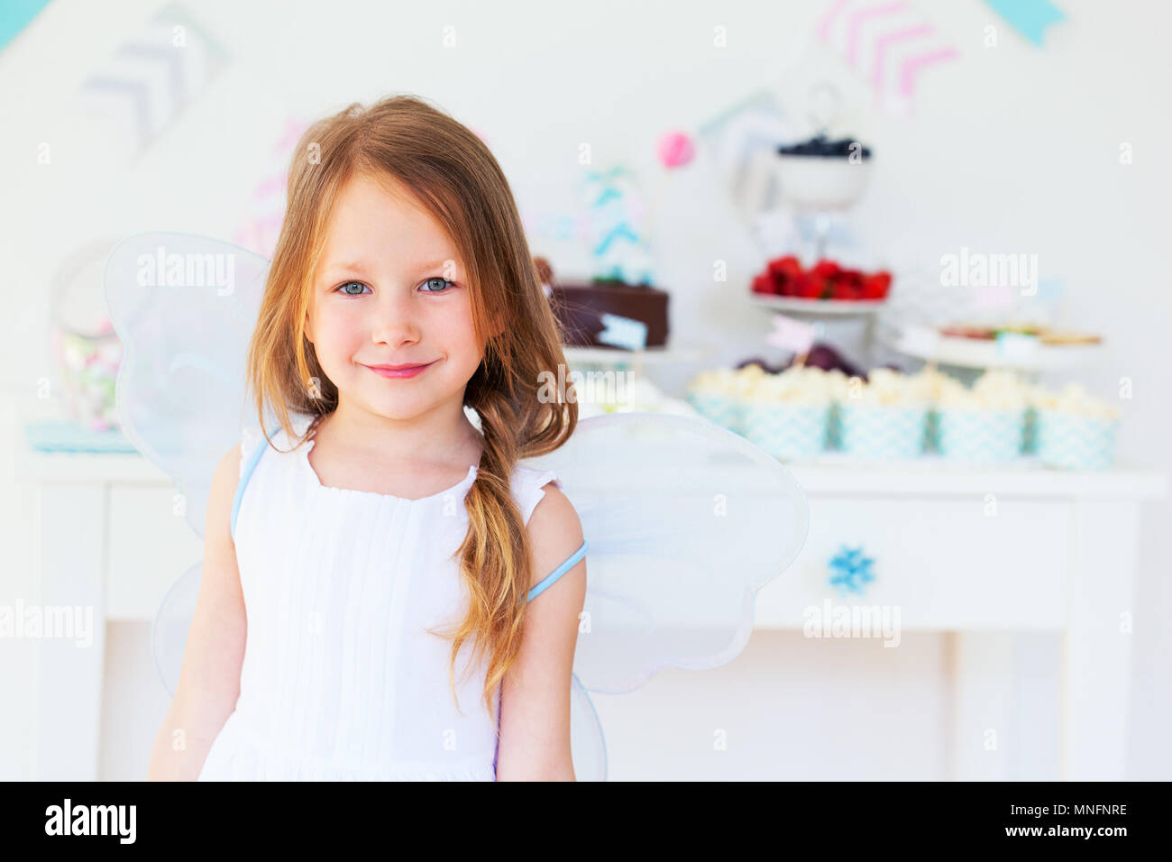 Adorable kleine Fee Mädchen mit Flügeln auf einer Geburtstagsfeier in der Nähe von Dessert Tabelle Stockfoto