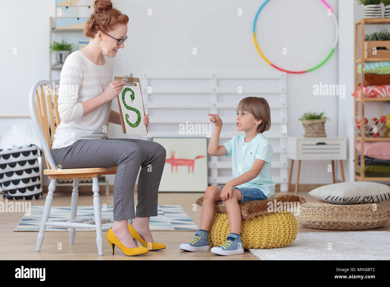 Junge sitzt auf einem gelben Pouf üben die richtige Aussprache während einer Lektion mit logopädin Stockfoto