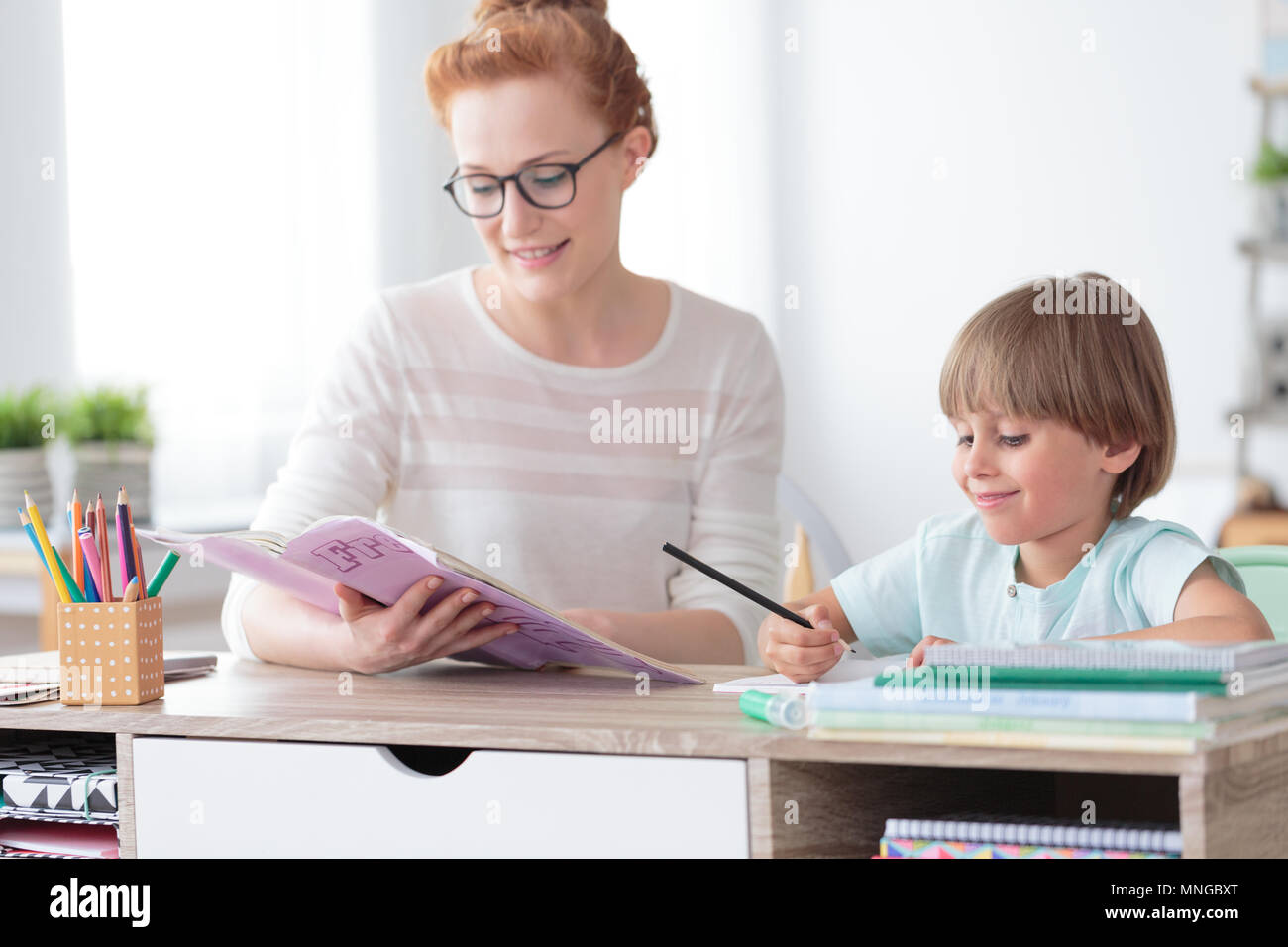 Mathelehrer Übungen aus der Arbeitsmappe mit Jungen glückliche junge Beim am Schreibtisch im Klassenzimmer sitzen Stockfoto