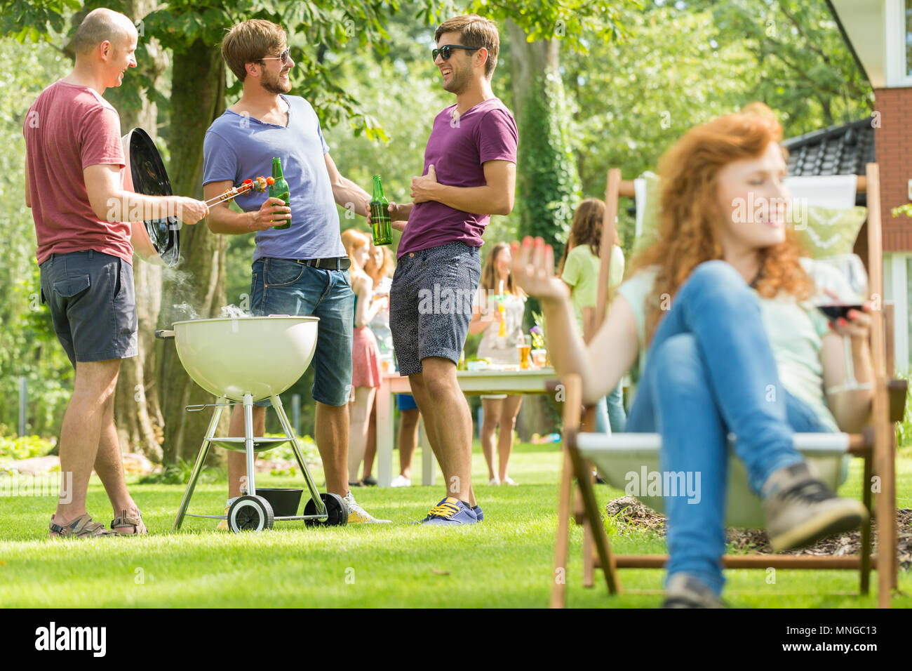Männer trinken Bier und Grillen, Mädchen sitzen Liegestuhl Stockfoto