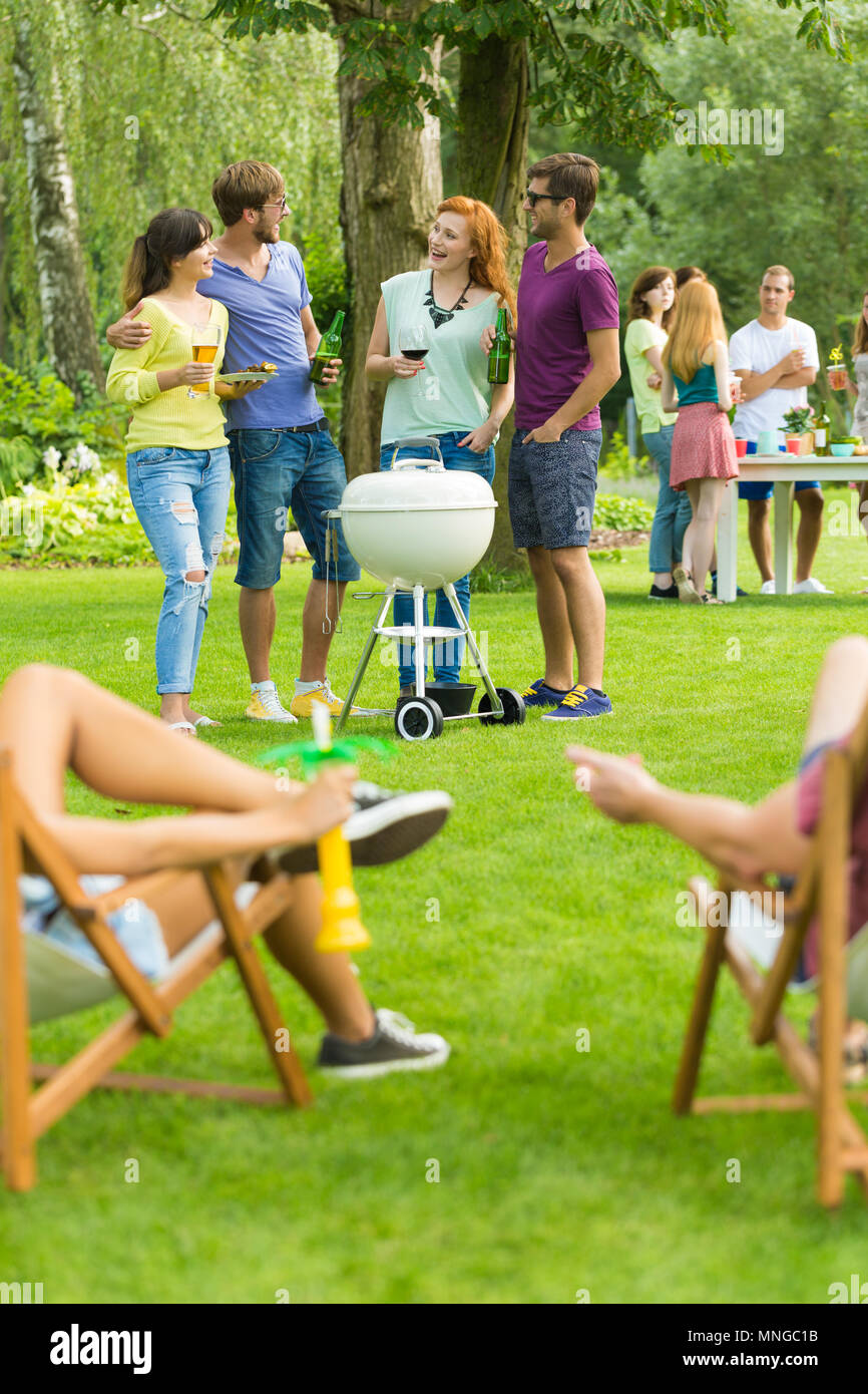 Freunde stand neben Grill, Menschen, die sich auf Liegestühlen Stockfoto