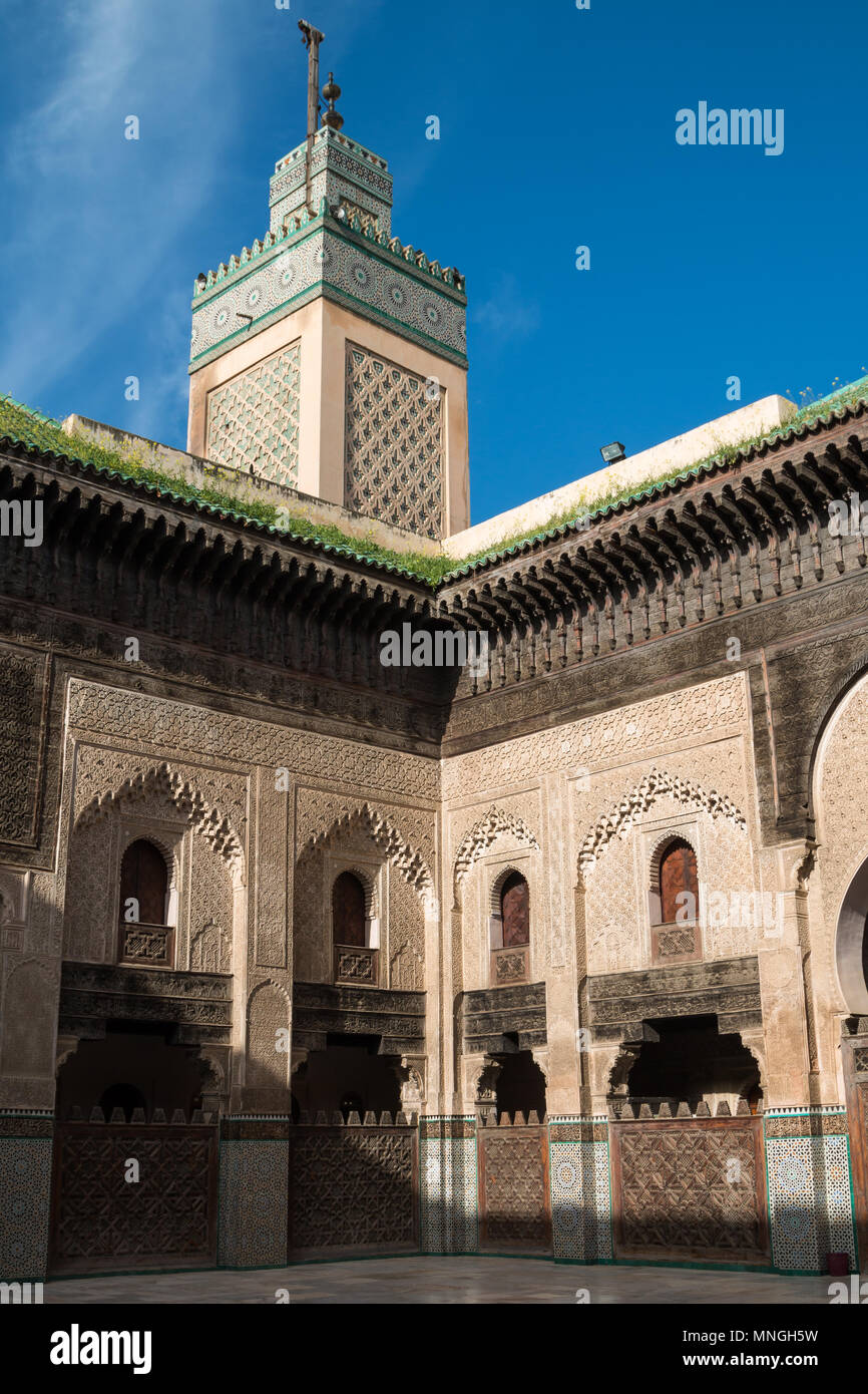 Blick vom Hof der islamischen Schule Madrasa Bou Inania, Fes, Marokko. Details der Architektur und der Turm der Moschee. Blauer Himmel, weiße Wolke. Stockfoto