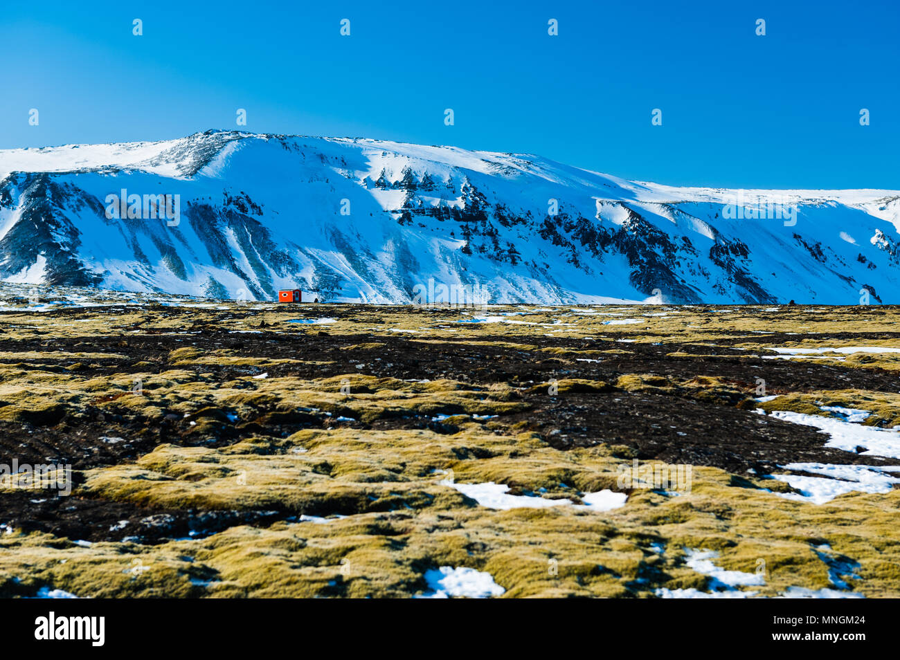 Lonely orange Kabine in unwirtlichen Landschaft vor der schneebedeckten Berge, Island april 2018 Stockfoto