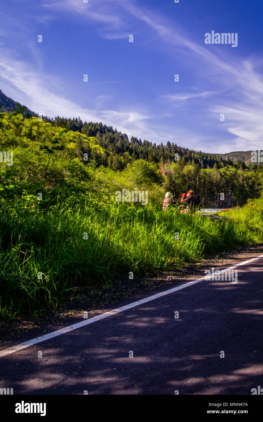 Wanderer gönnen Sie sich eine Pause und trinken Sie etwas, wo der Fluss die Straße trifft. Stockfoto