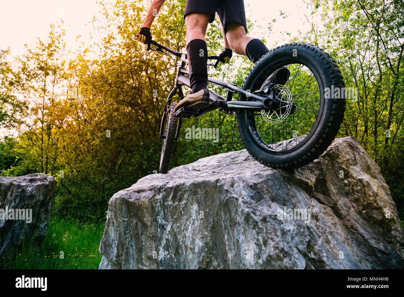 Radfahrer Beine auf einen Versuch mit dem Fahrrad oben auf einem Felsen bei Sonnenuntergang. Konzept der Extreme Sport Stockfoto