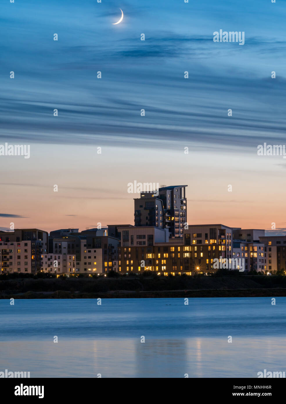 Leith Harbour, Edinburgh, Schottland, Großbritannien, 17. Mai 2018. Wetter in Großbritannien: Ein ungewöhnliches nächtliches Himmelsereignis eines wunderschön schlanken Halbmondes, das unmittelbar nach einem herrlichen Sonnenuntergang zu sehen ist und über den Hafen des Eingangsbecken in Richtung des Hochhauses blickt, beleuchtete Fenster von Apartmentgebäuden von Platinum Point in Newhaven, mit einer Spiegelung des Turmblocks im Wasser Stockfoto