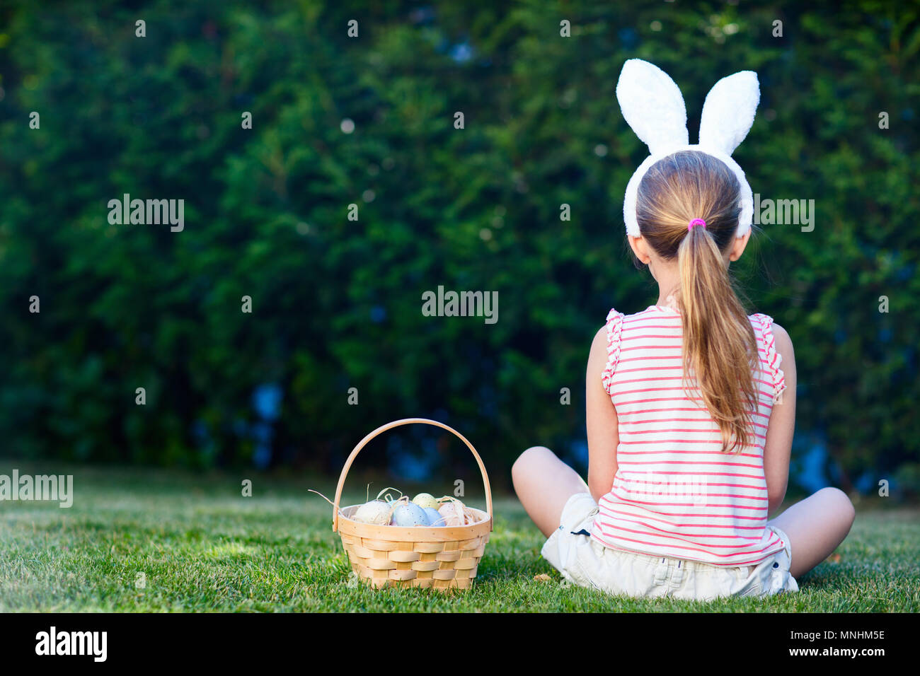 Rückansicht eines kleinen Mädchens tragen Häschenohren mit einem Korb von bunten Ostereier im Freien auf Frühling Stockfoto