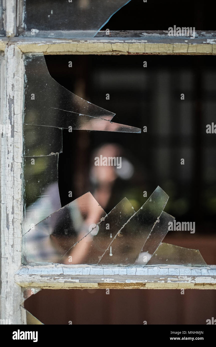 Partielle Reflexion eines jungen Mannes in Shattered Glas eines zerbrochenen Fensters in ein verlassenes Haus Stockfoto