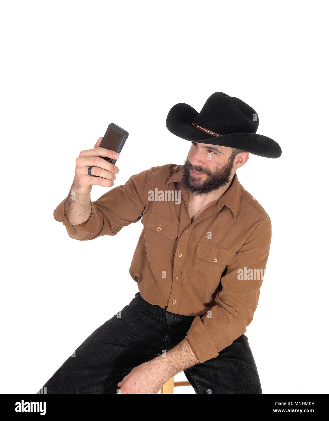 Ein junger stattlicher Mann trägt einen schwarzen Cowboyhut und braunes Hemd mit einem selfie mit seinem Handy, auf weißem Hintergrund Stockfoto
