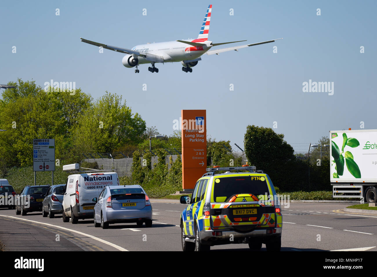 American Airlines Boeing 777 Jet Flugzeug landet am London Heathrow Airport UK in blauem Himmel über Polizeiauto und Parkschild Stockfoto