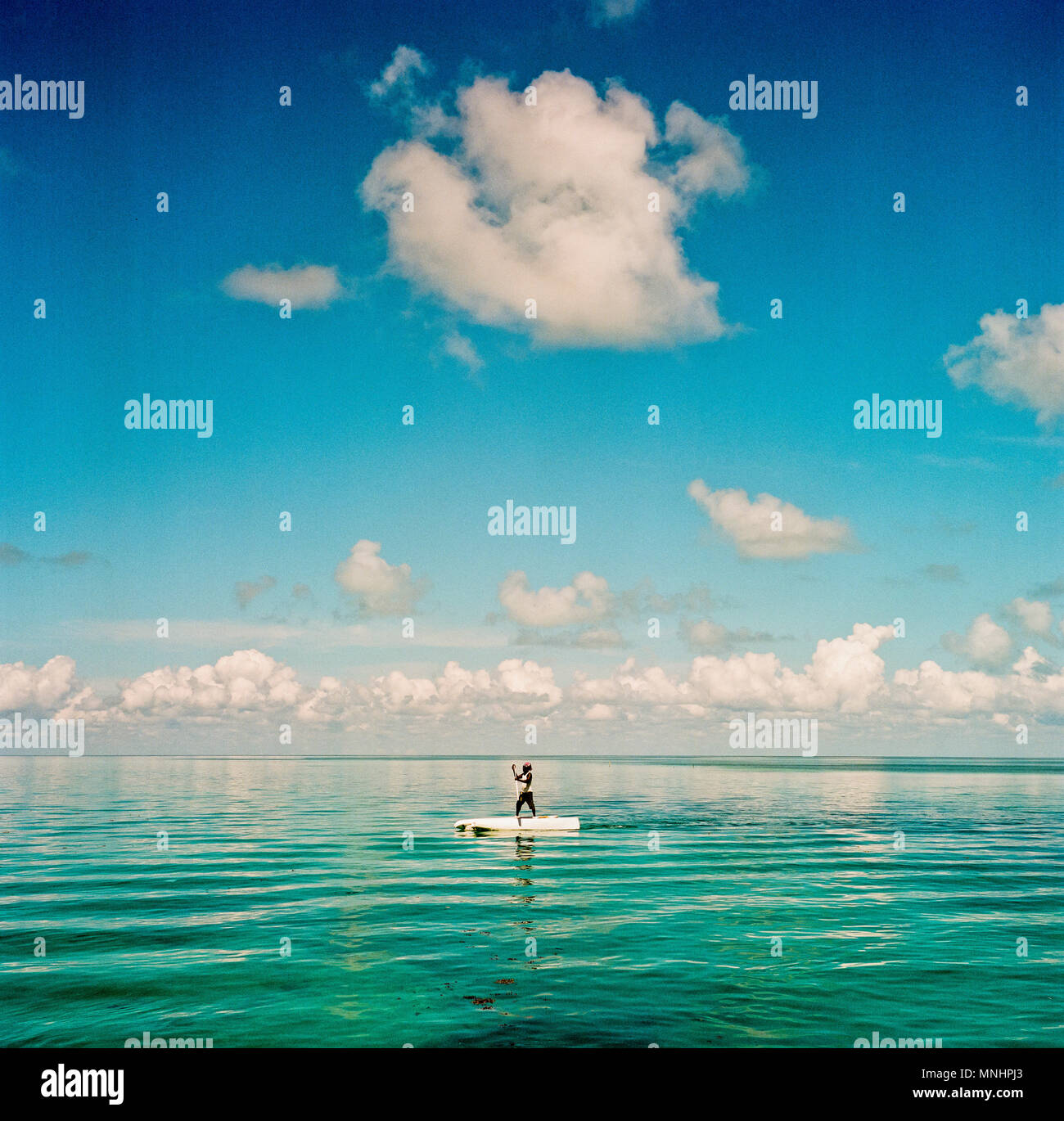Weiße Wolken über Mann Paddeln über offenes Wasser in der Nähe der Küste der Insel Caye Caulker, Belize, Belize Stockfoto