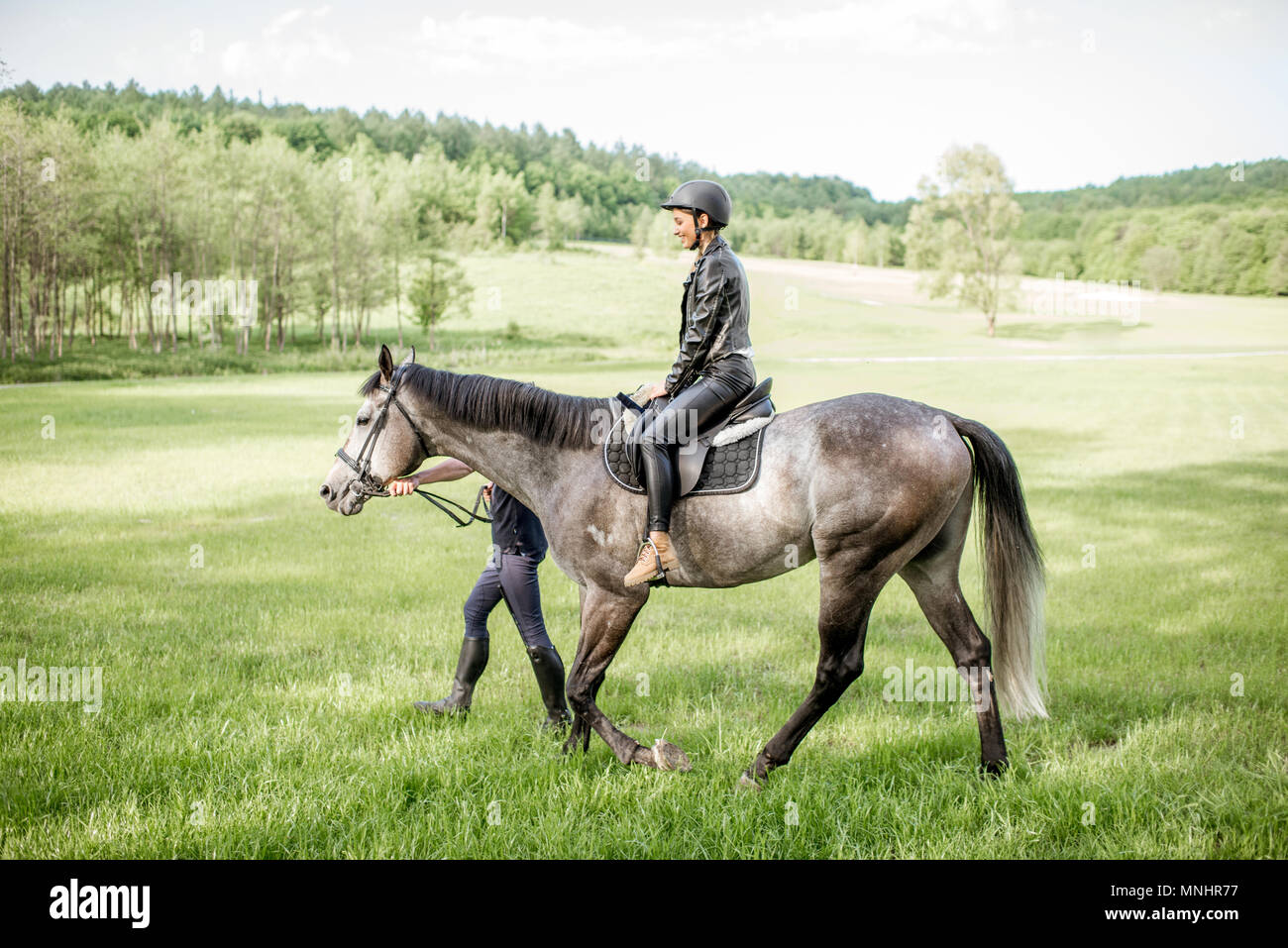 Mann ein Pferd mit Frau Reiter auf dem schönen grünen Wiese während der sonnigen Wetter Stockfoto