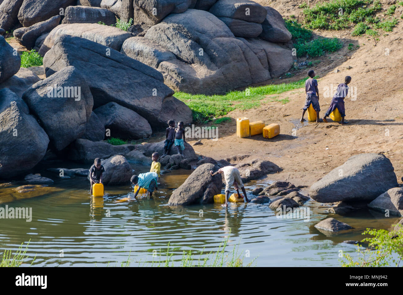 Nicht identifizierte junge Kinder füllen gelbes Wasser Behälter am Fluss Stockfoto