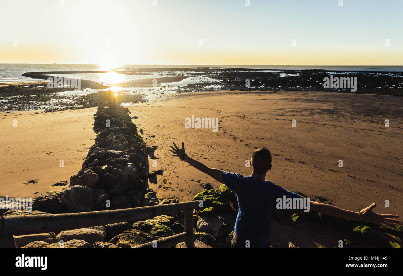 Junger Mann mit ausgestreckten Armen bei Sonnenuntergang am Strand von Sanlucar de Barrameda Stockfoto
