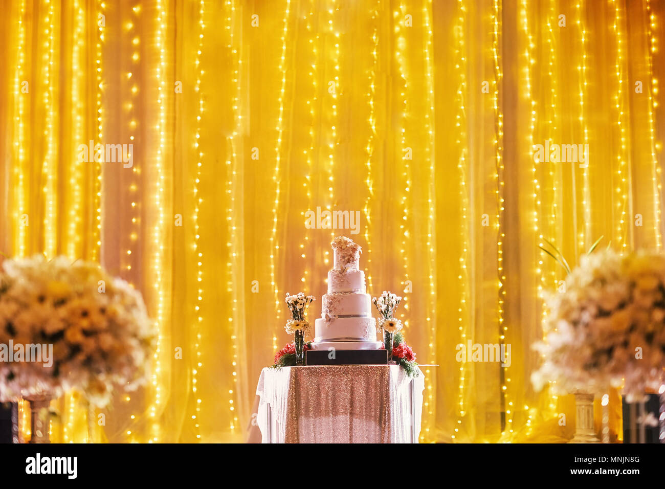 Schöne vier Schichten Hochzeit auf dem Tisch auf der Bühne Dekoration mit LED-Leuchte in Gelb golden Thema mit Teil der biuquet Blume verschwommen im Vordergrund Stockfoto