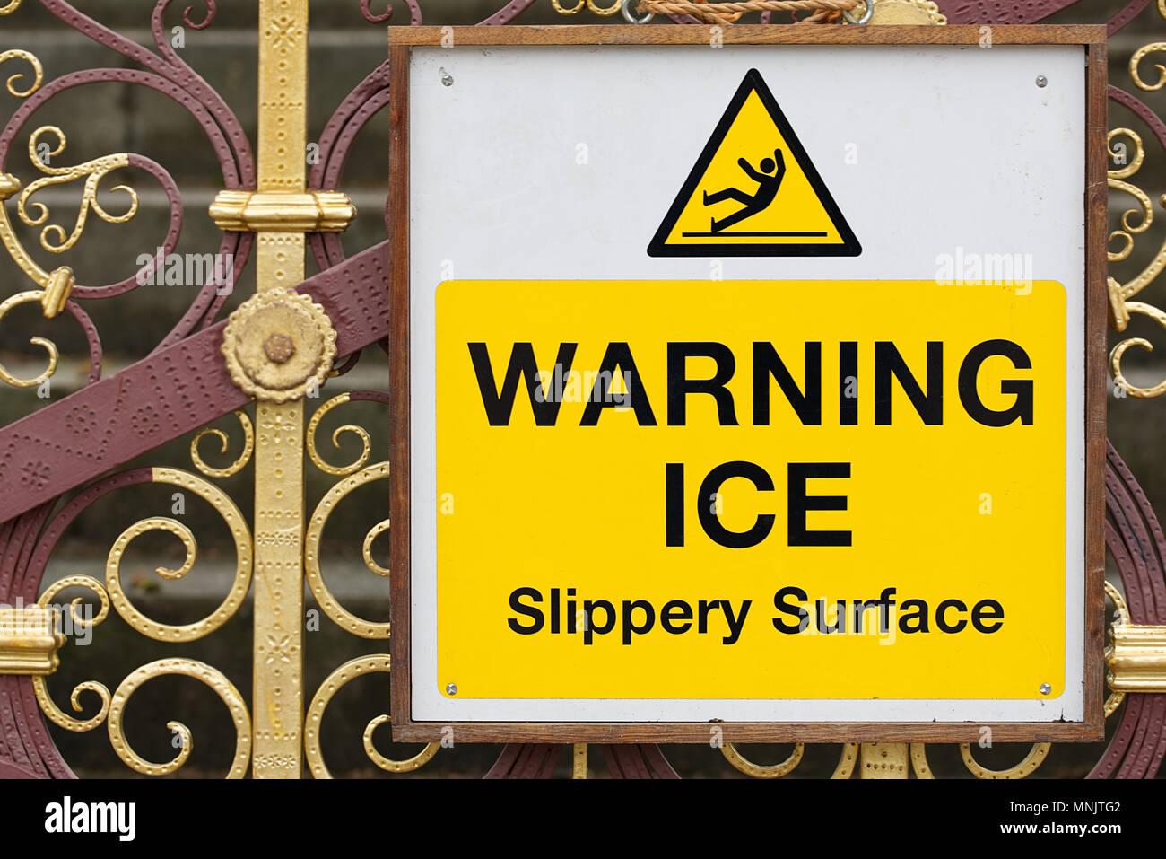 Warnung Eis rutschige Oberfläche Zeichen schwarzer Text auf gelbem und weißem Hintergrund mit Symbol eines Mannes Ausrutschen auf Eis auf schmiedeeiserne Tore. Winter einfrieren Stockfoto