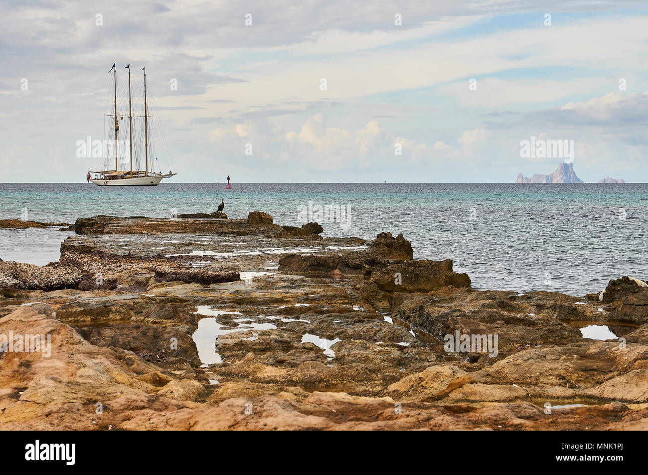 Einen verankerten klassische Segelboot mit roter Fahne Flagge mit einer europäischen Shag (Phalacrocorax aristotelis) Es Vedrá Inselchen (Formentera, Balearen, Spanien) Stockfoto