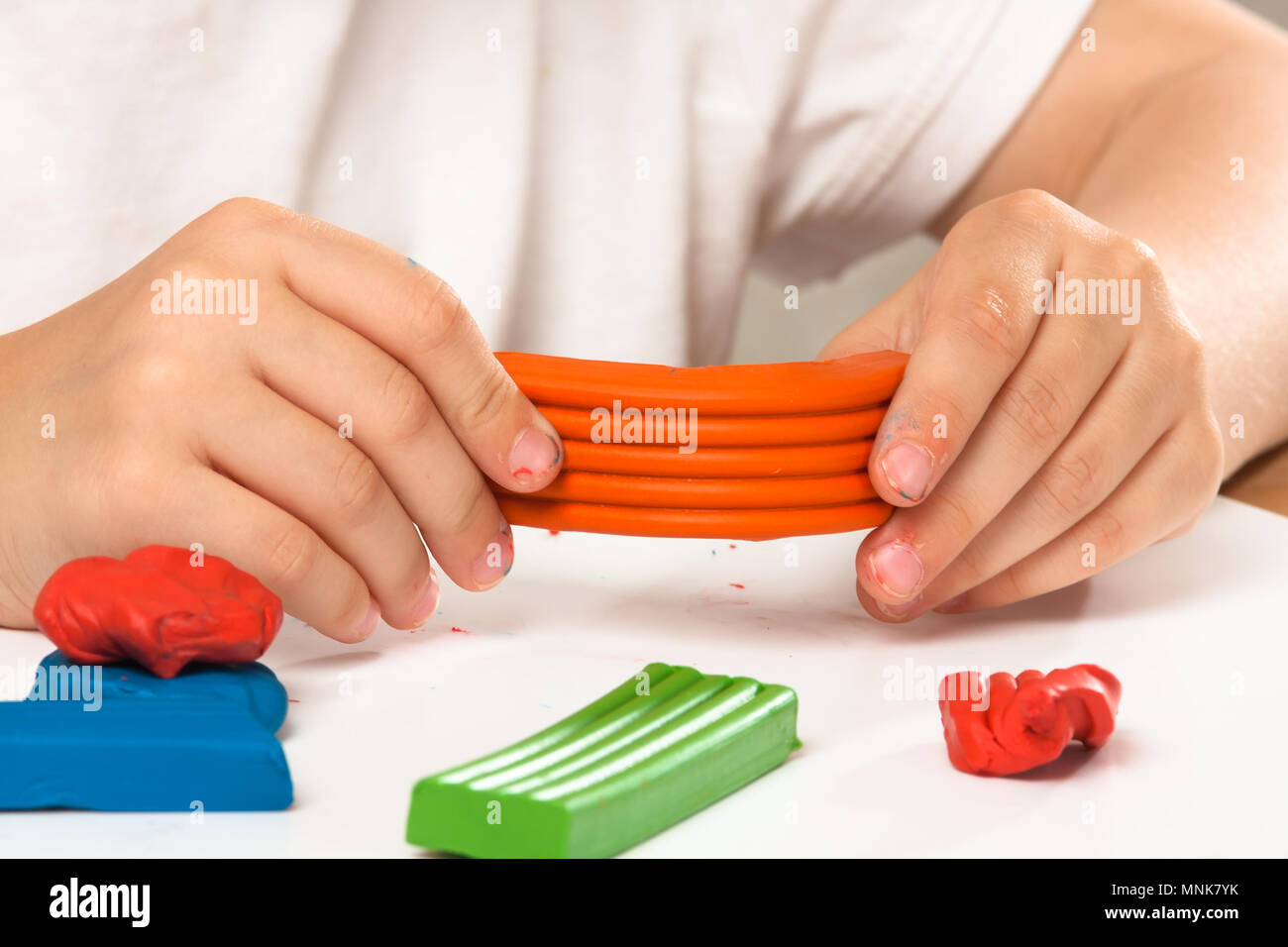 Die Hände des Kindes Spritzgießen von orange Knetmasse auf den Tisch Stockfoto
