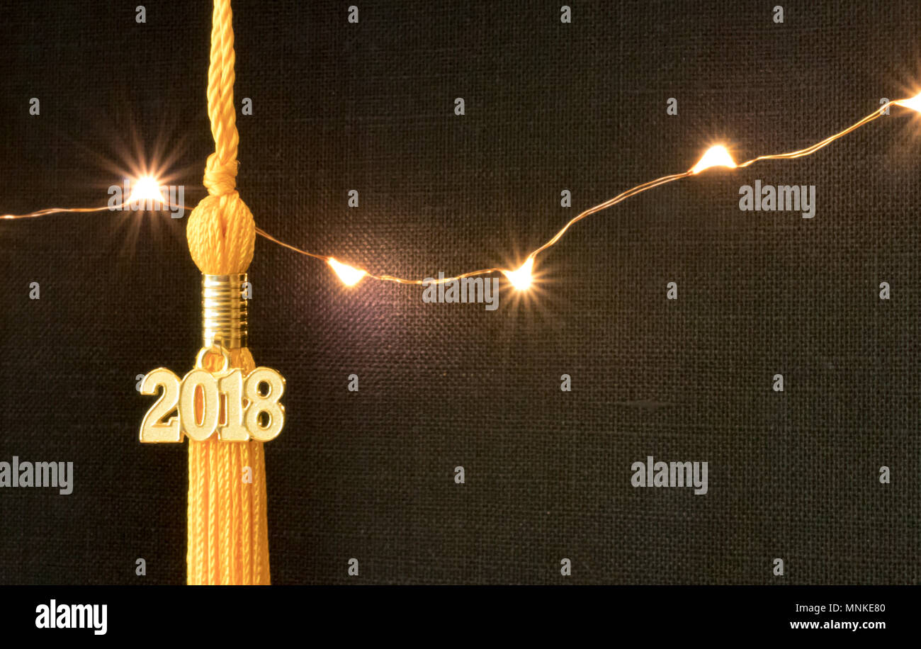Klasse von 2018. Gold Quaste drop Graduierung kleid Zubehör und Andenken vor einem schwarzen Hintergrund und Leuchten. Iconic Symbol der akademischen Leistung. Stockfoto