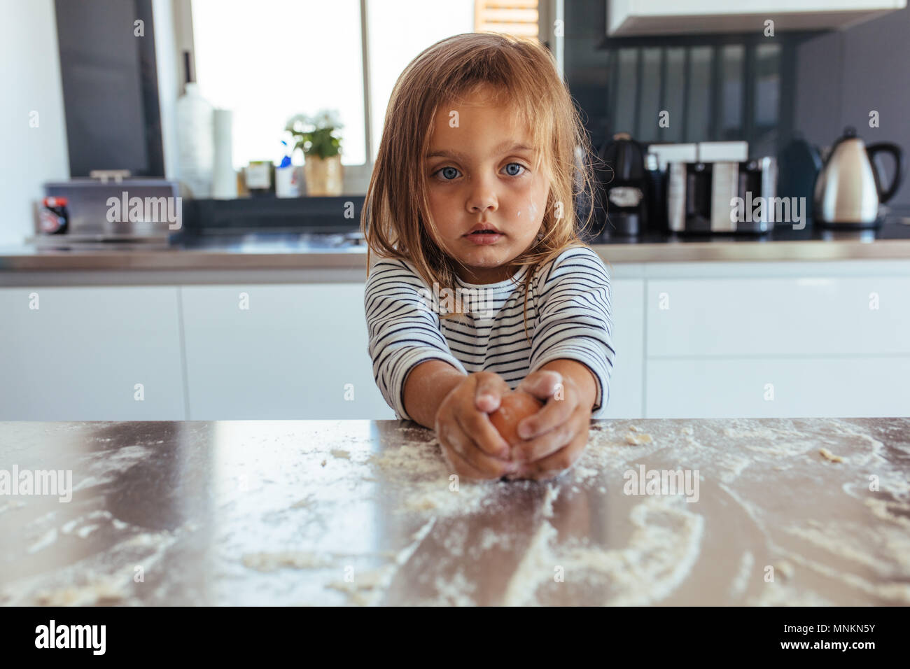 Unschuldige kleine Mädchen bricht ein Ei mit Mehl auf die Arbeitsplatte in der Küche. Kleines Mädchen backen in der Küche zu Hause. Stockfoto