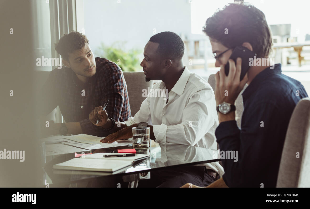 Unternehmer diskutieren Arbeit am Konferenztisch Sitzen im Büro. Zwei Männer diskutieren, arbeiten, während ein anderer Mann Gespräch am Handy ist. Stockfoto
