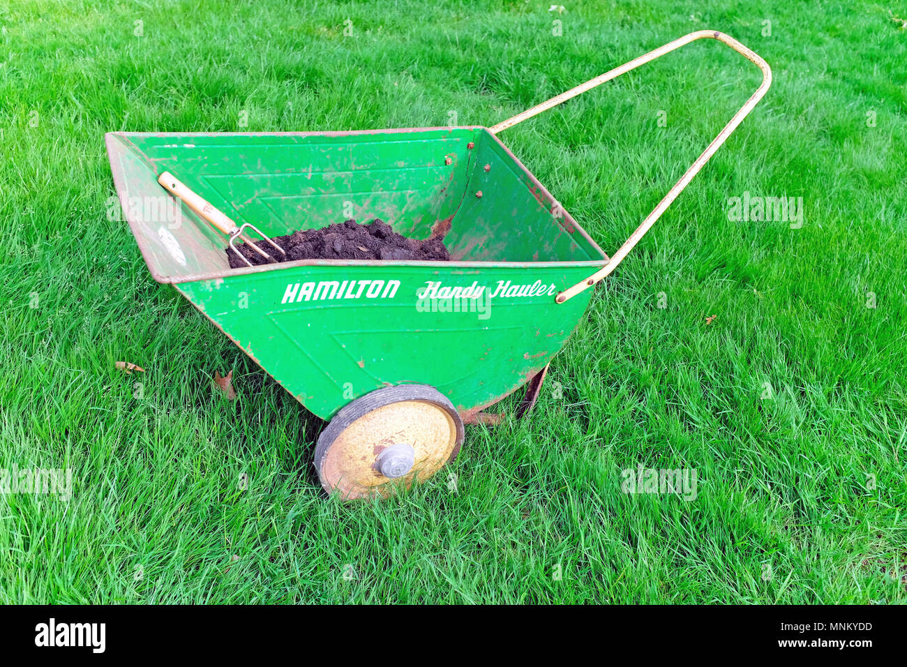 Helle grüne alte Hamilton handliche Verkehrsunternehmer mit Kompost, Erde, und ein Garten Werkzeug innen. Stockfoto