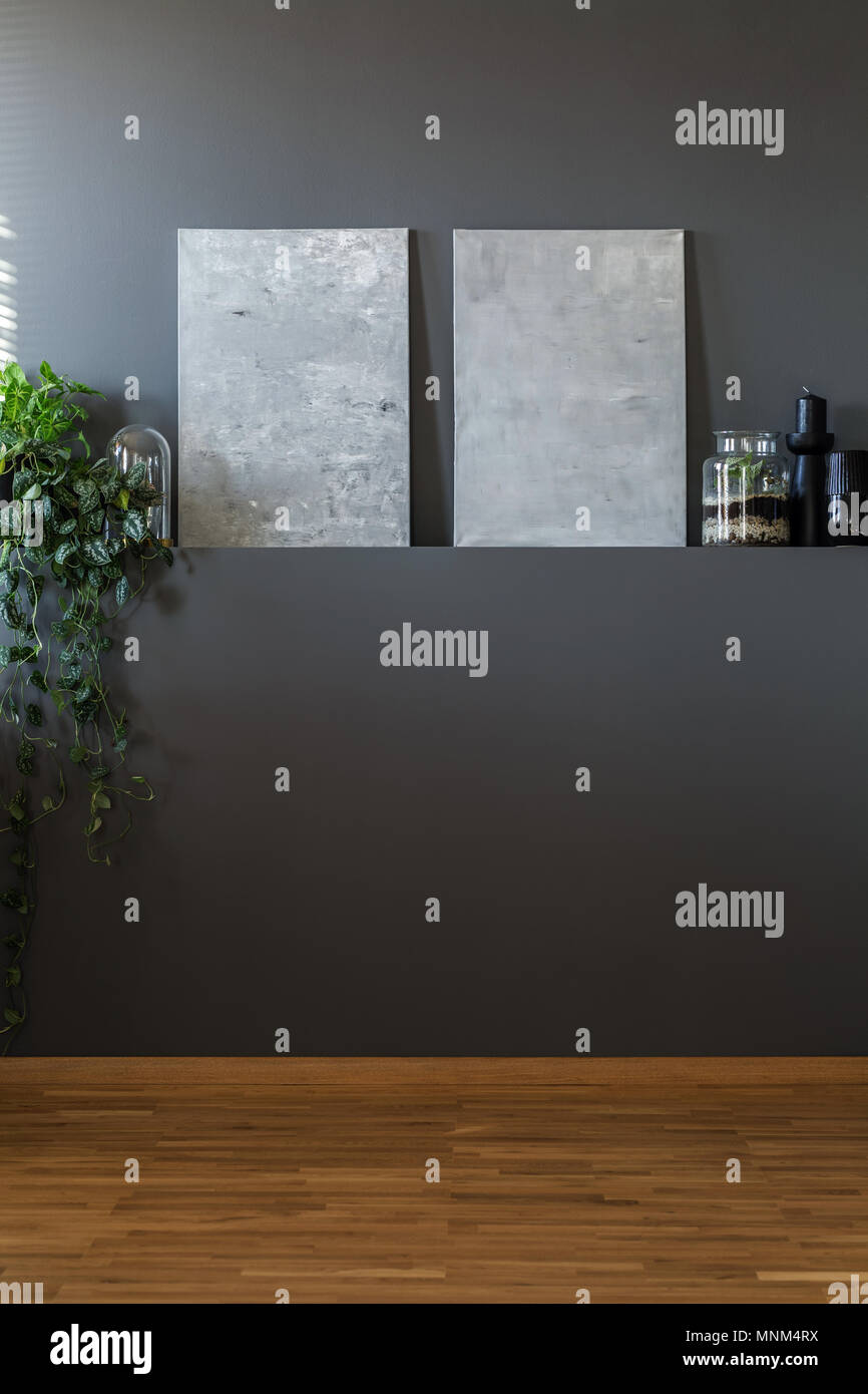 Abstrakte graue Leinwand und Ivy Anlage hängen von einer leeren dunklen Mauer in einem minimalistischen Wohnzimmer Innenraum Stockfoto