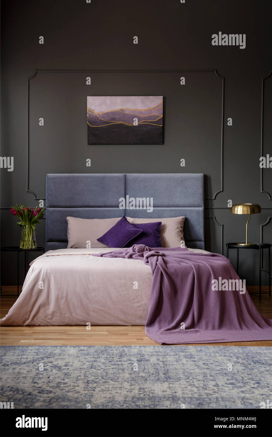 Violette Decke auf dem Bett mit Kopfteil in geräumigen Schlafzimmer Innenraum mit Malerei auf graue Wand Stockfoto