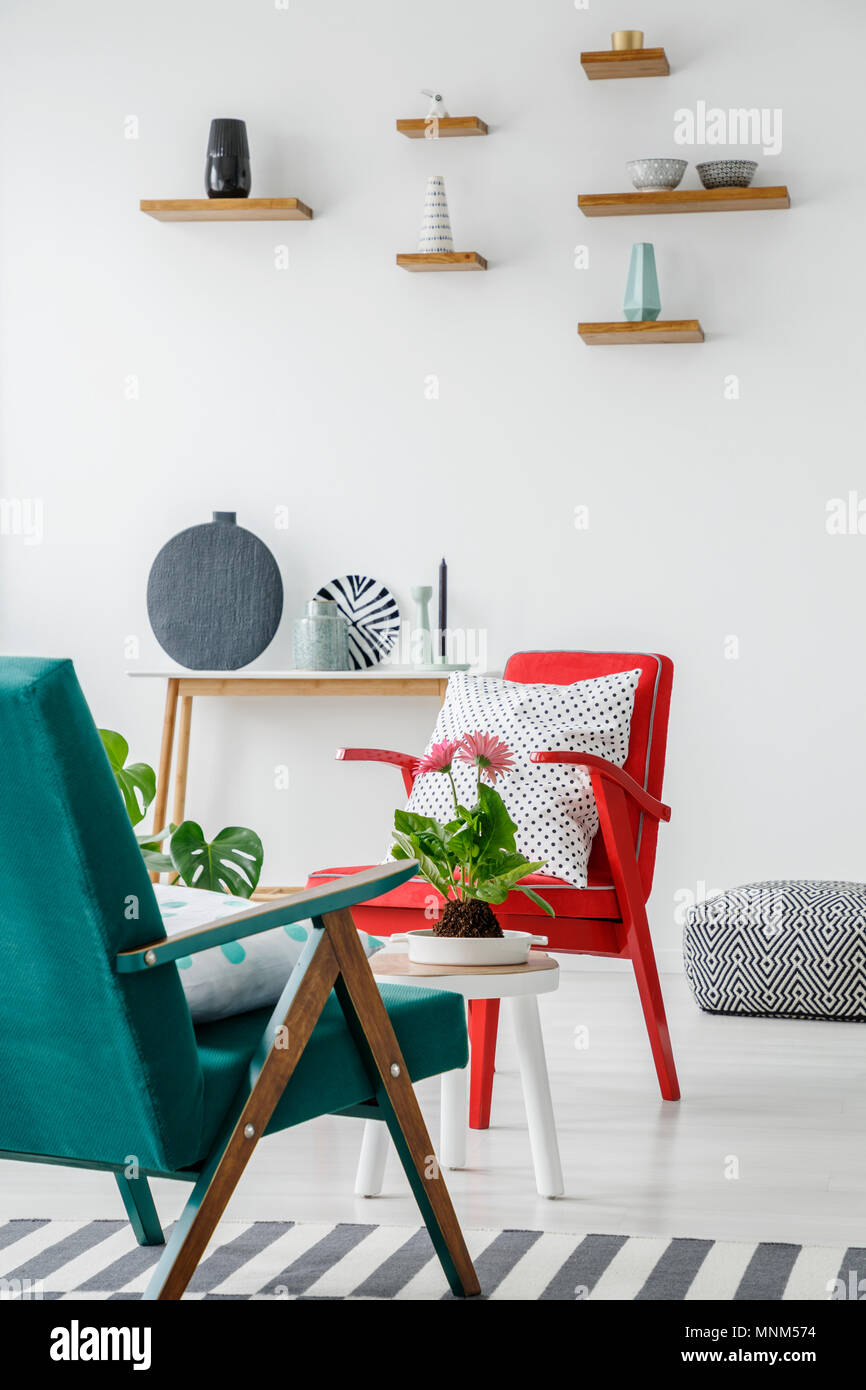 Seite Winkel von grünen und roten Sesseln in ein Wohnzimmer mit Tisch, Regale, Pflanzen und Vasen set Stockfoto