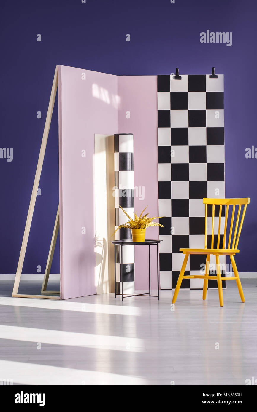 Gelbe Stuhl gegen Schachbrettmuster Wand in lila Foto Studio Interieur mit Anlage auf Tisch Stockfoto