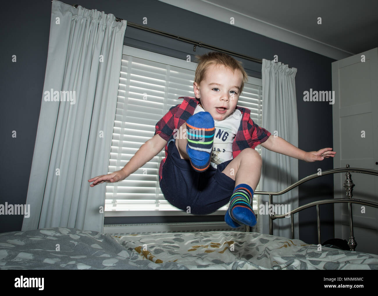 Ein kleiner Junge springt auf ein Bett in einem Schlafzimmer/Kind sprang auf dem Bett Stockfoto