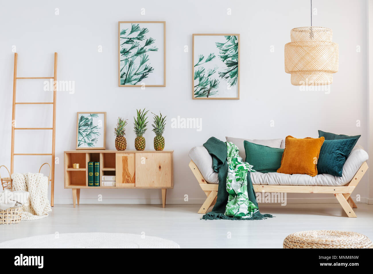Ananas auf rustikalen Schrank zwischen Leiter und beige Sofa mit grün und orange Kissen im Wohnzimmer Stockfoto