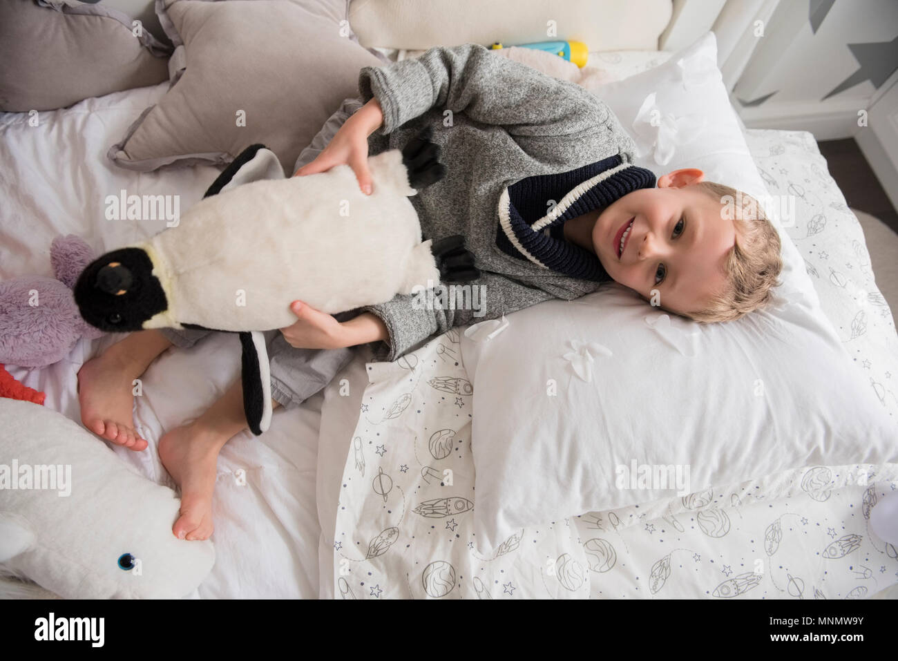 Little Boy (4-5) im Bett liegend mit Spielzeug in den Händen Stockfoto